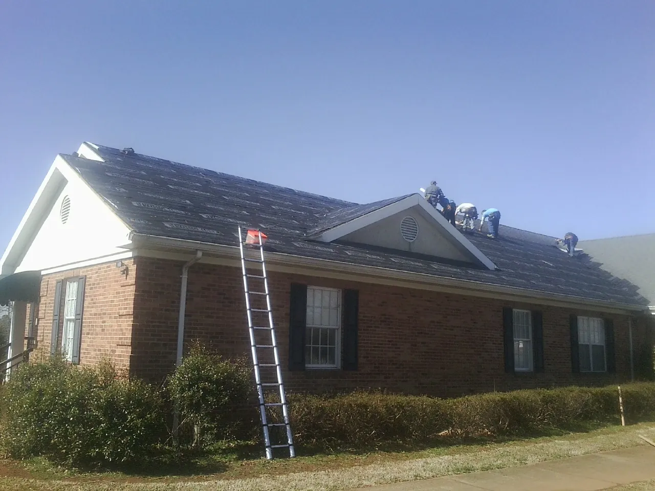 Crew tearing shingles off a brick ranch roof with a ladder set — Emergency Roof Repair work by our crew in Johnstown