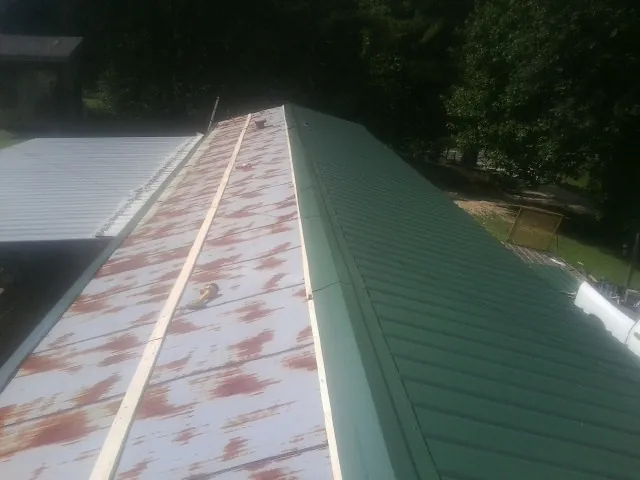Old rusted panels beside newly installed green metal roofing — Wind Damage Roof Repair by Roofing Brothers in Johnstown
