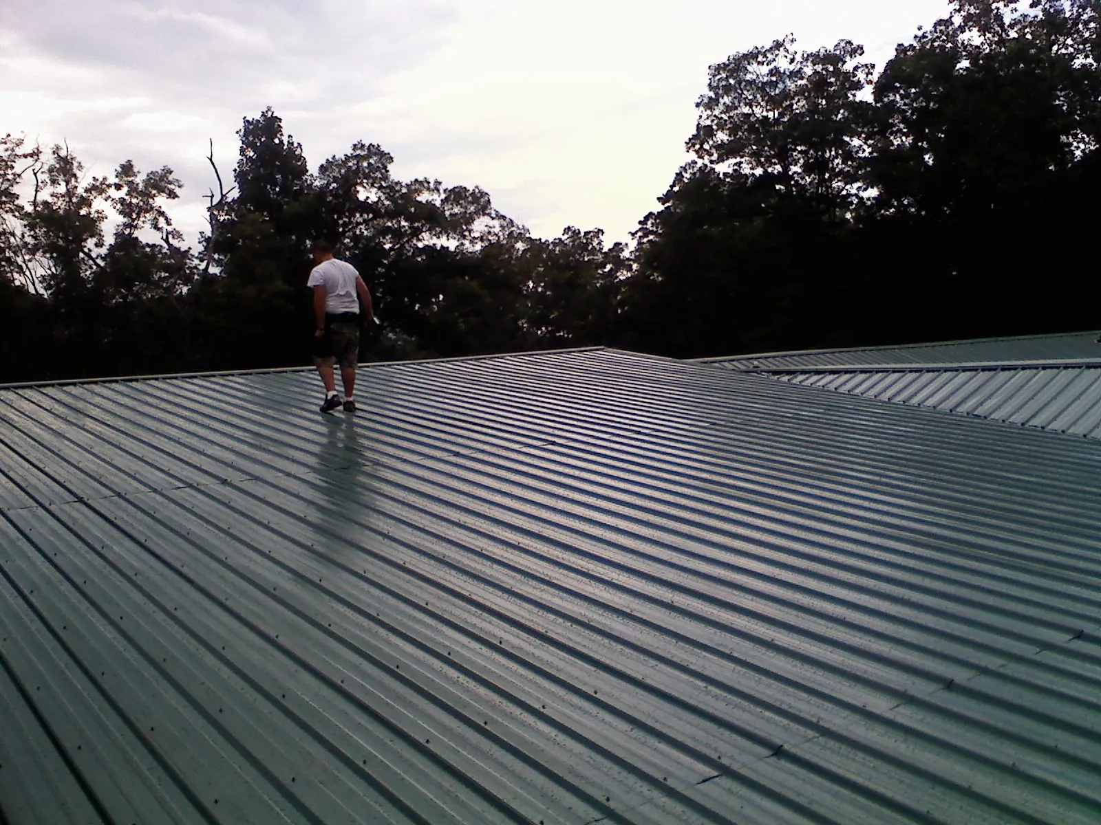 Roofer walking a wide expanse of new green metal roofing in Johnstown