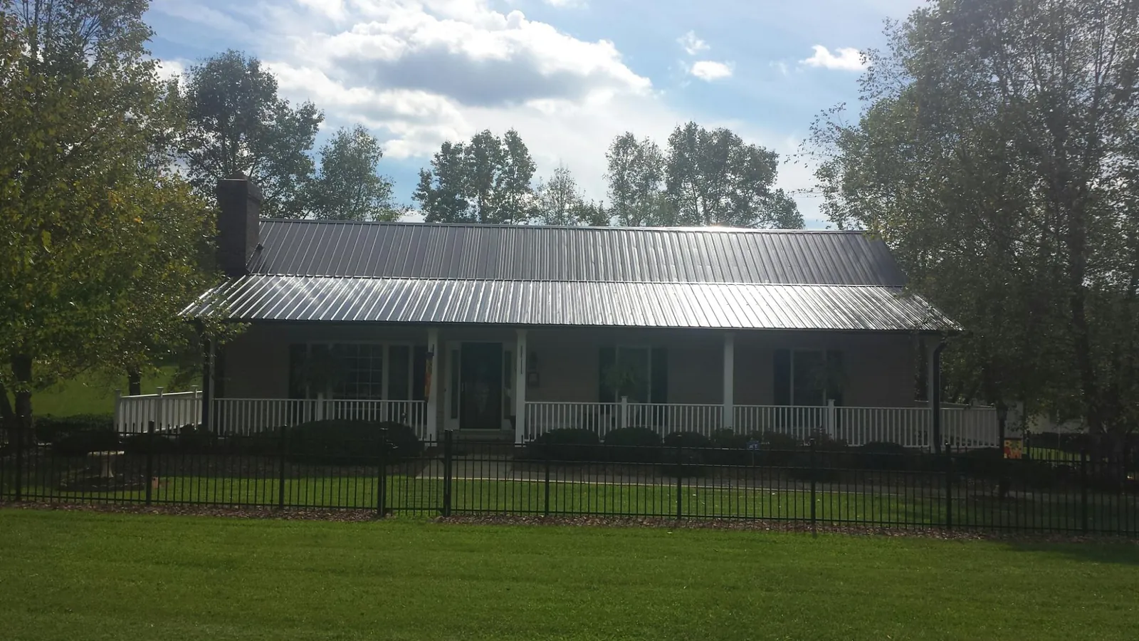 Gray metal roof on a brick ranch with a full width front porch — Gutter Guard Installation work by our crew in Johnstown
