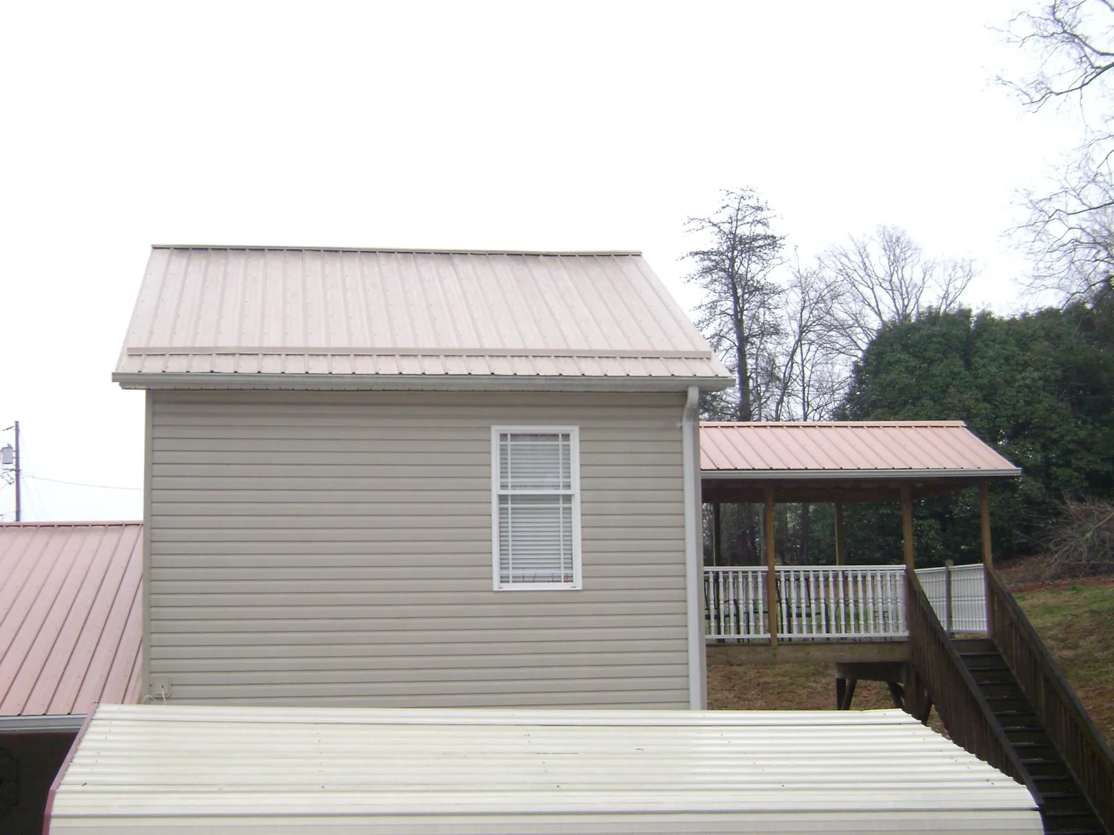 Tan metal roofs on a two story addition and attached porch, from a Roof Replacement job in Johnstown